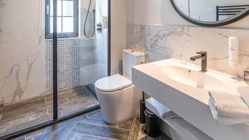 Un baño moderno con ducha de vidrio, un espejo grande y suelo de mármol.