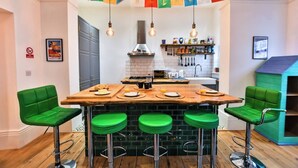 Cuina amb una illa central, tamborets de bar, llums penjants i un fanal de colors.