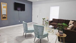 A modern living room with a flat-screen TV, two light blue armchairs, a brown sofa, and a glass coffee table. - Beautiful apartment 9 min to Mercedes outlets (Weslaco)