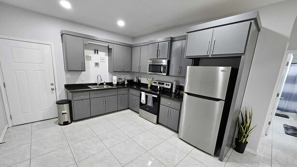 A modern kitchen with grey cabinets, stainless steel appliances, and a tiled floor. - Beautiful apartment 9 min to Mercedes outlets (Weslaco)
