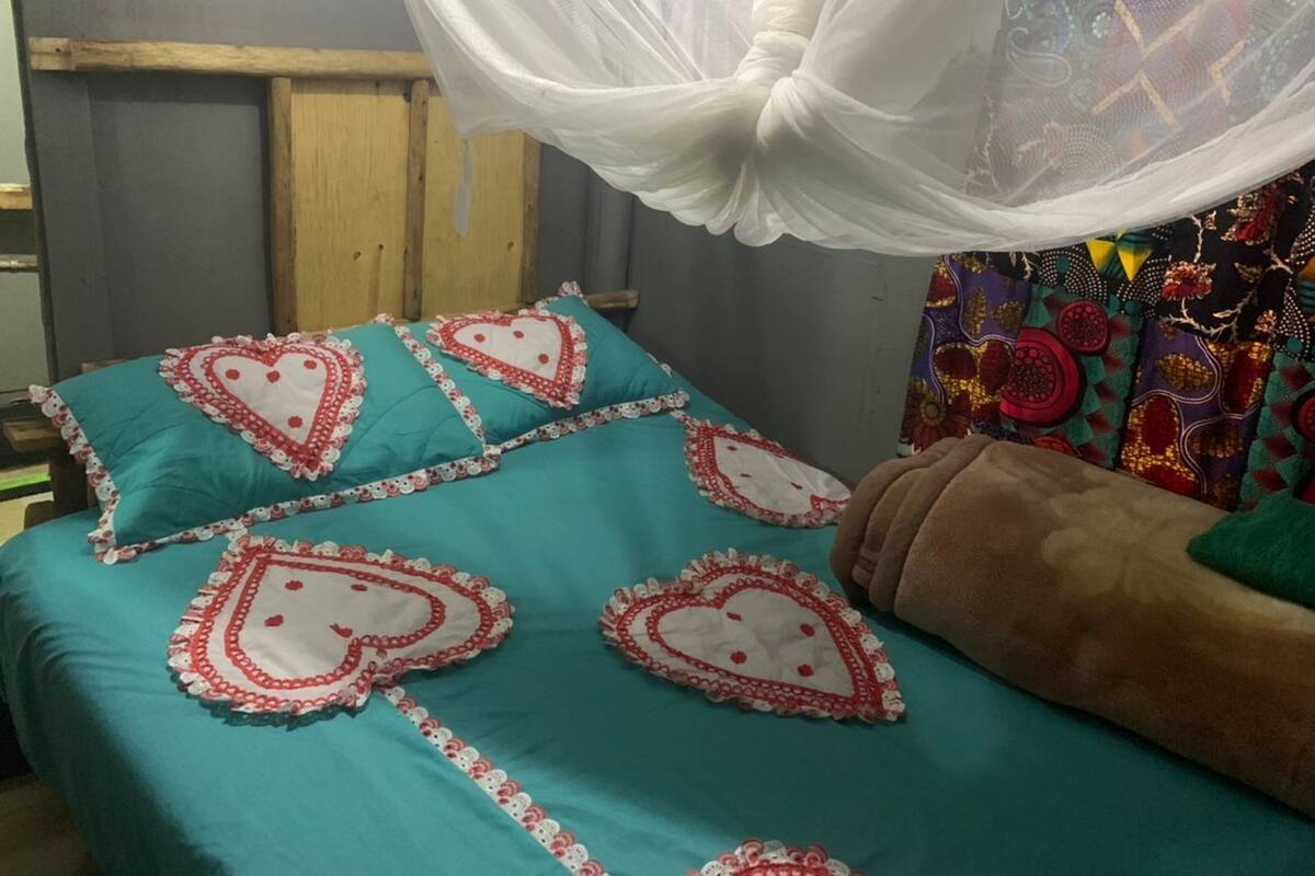 A bed with teal bedding and heart-shaped pillows, a wooden headboard, and a colorful curtain.