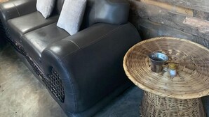 Une pièce chaleureuse avec un canapé en cuir noir et une table en osier.