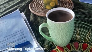 Une table avec une bouteille, une tasse et une assiette de fruits. Il y a des papiers et un téléphone intelligent sur la table.