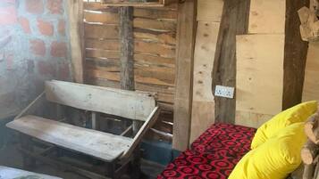 A rustic room with a wooden bench, a bed with a patterned blanket, and a shelf with books.
