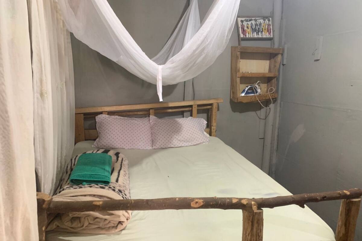 A single bed with a wooden headboard, a white canopy, and a small wooden shelf with a power outlet.