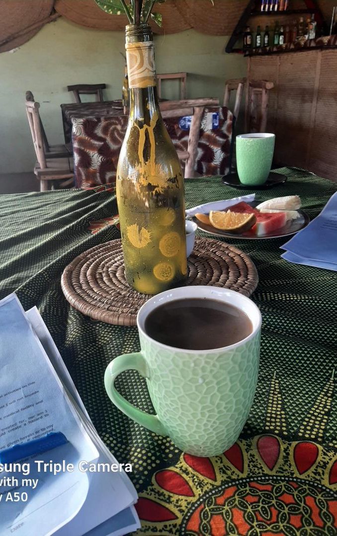 A table with a bottle, a cup, and a plate with fruit. There are papers and a smartphone on the table.