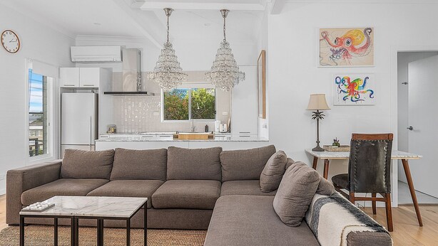 Una sala de estar moderna con un sofá modular, una mesa de centro de mármol y una cocina al fondo.