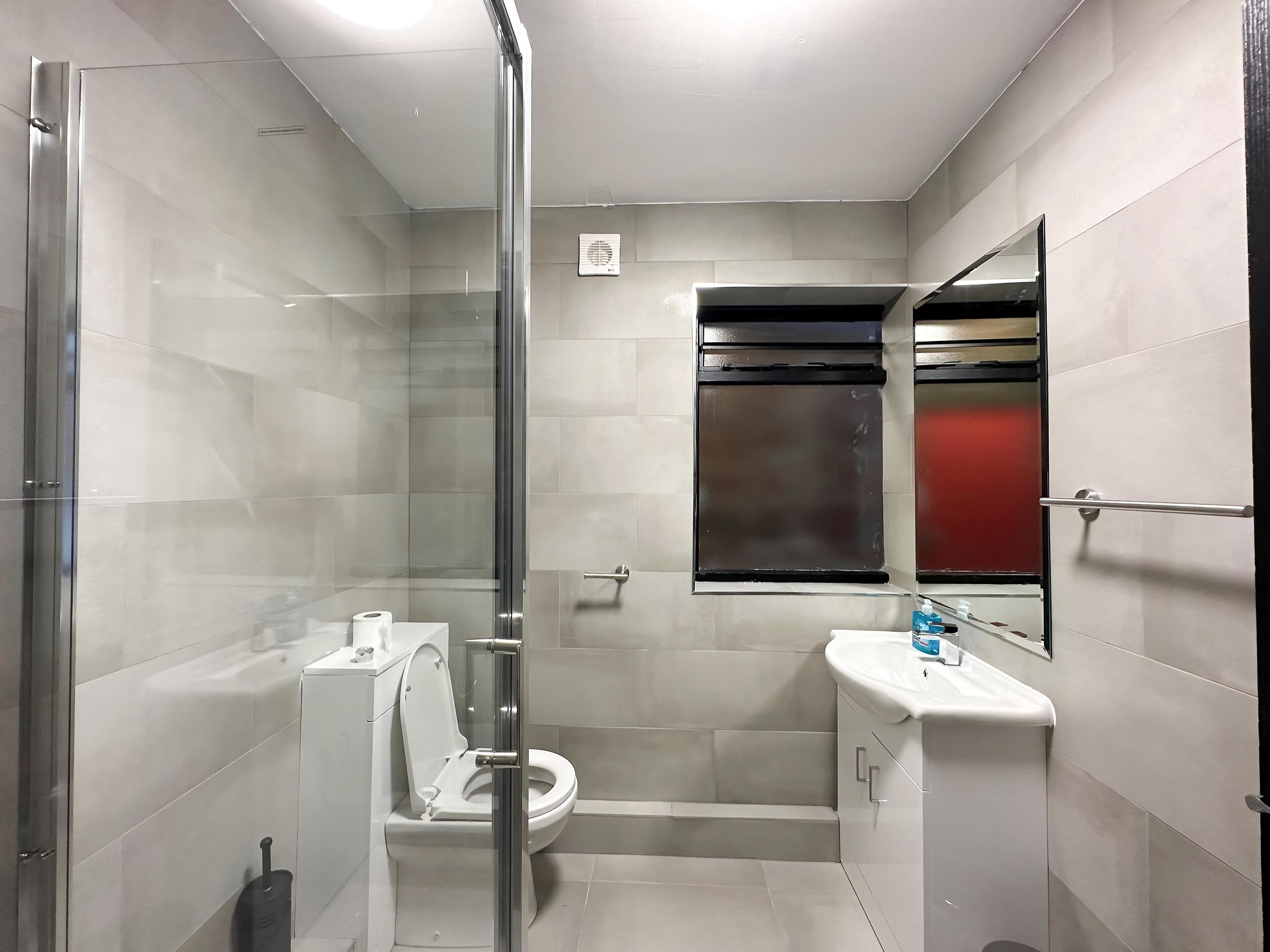 Un baño moderno con ducha vidriada, inodoro y lavamanos con espejo arriba.