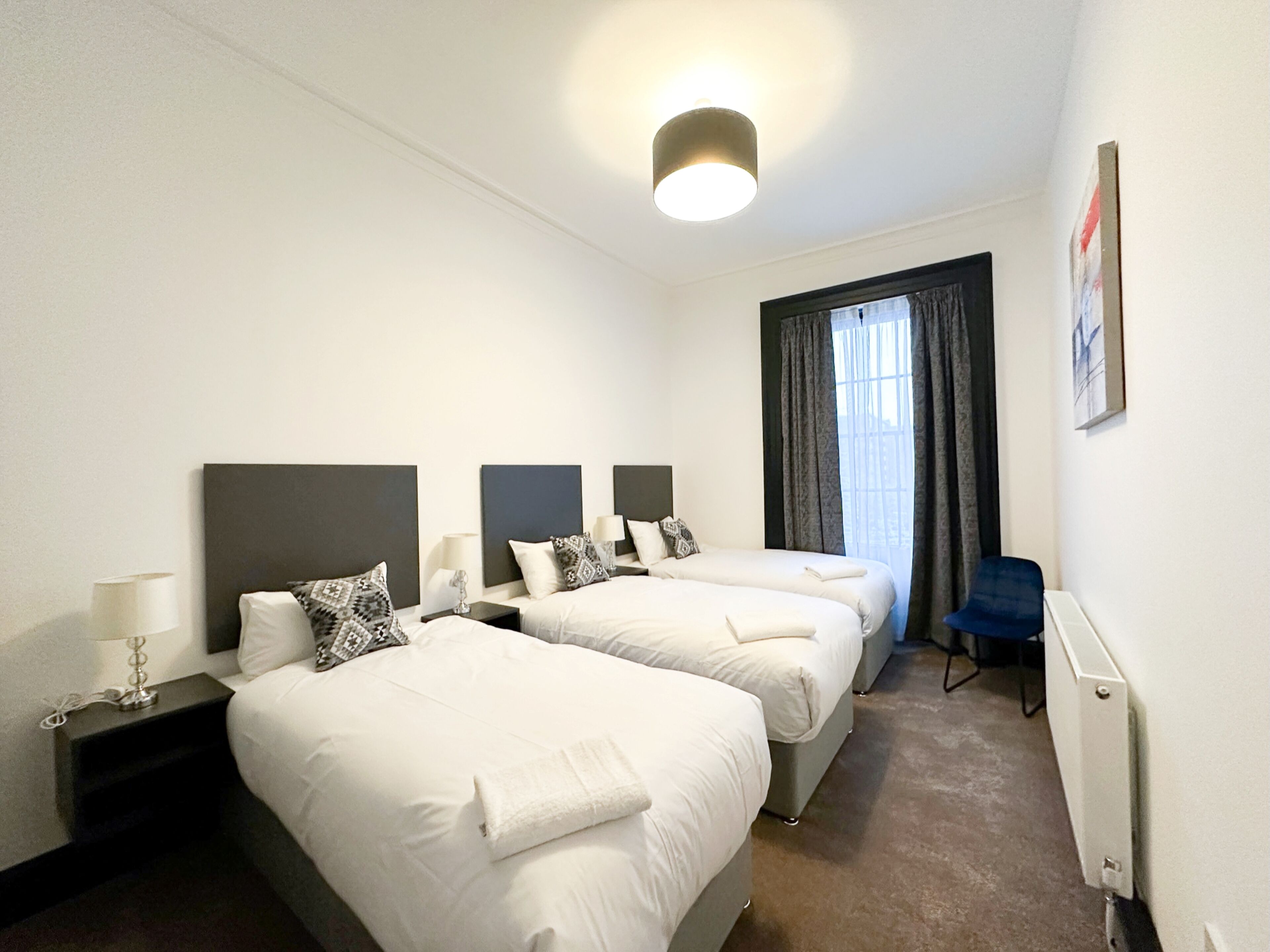 A hotel room with three beds, a desk, a chair, and a window with curtains.