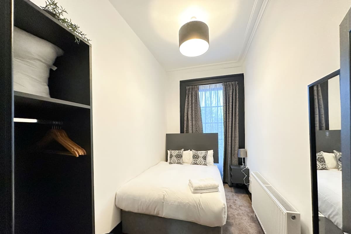 Quarto com cama, guarda-roupa, mesa de cabeceira, luminária e espelho.