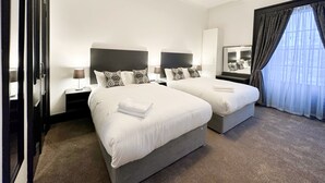 Ein Hotelzimmer mit zwei Betten, einem großen Spiegel, einer Deckenleuchte und Blick ins Freie durch ein mit Vorhängen versehenes Fenster.