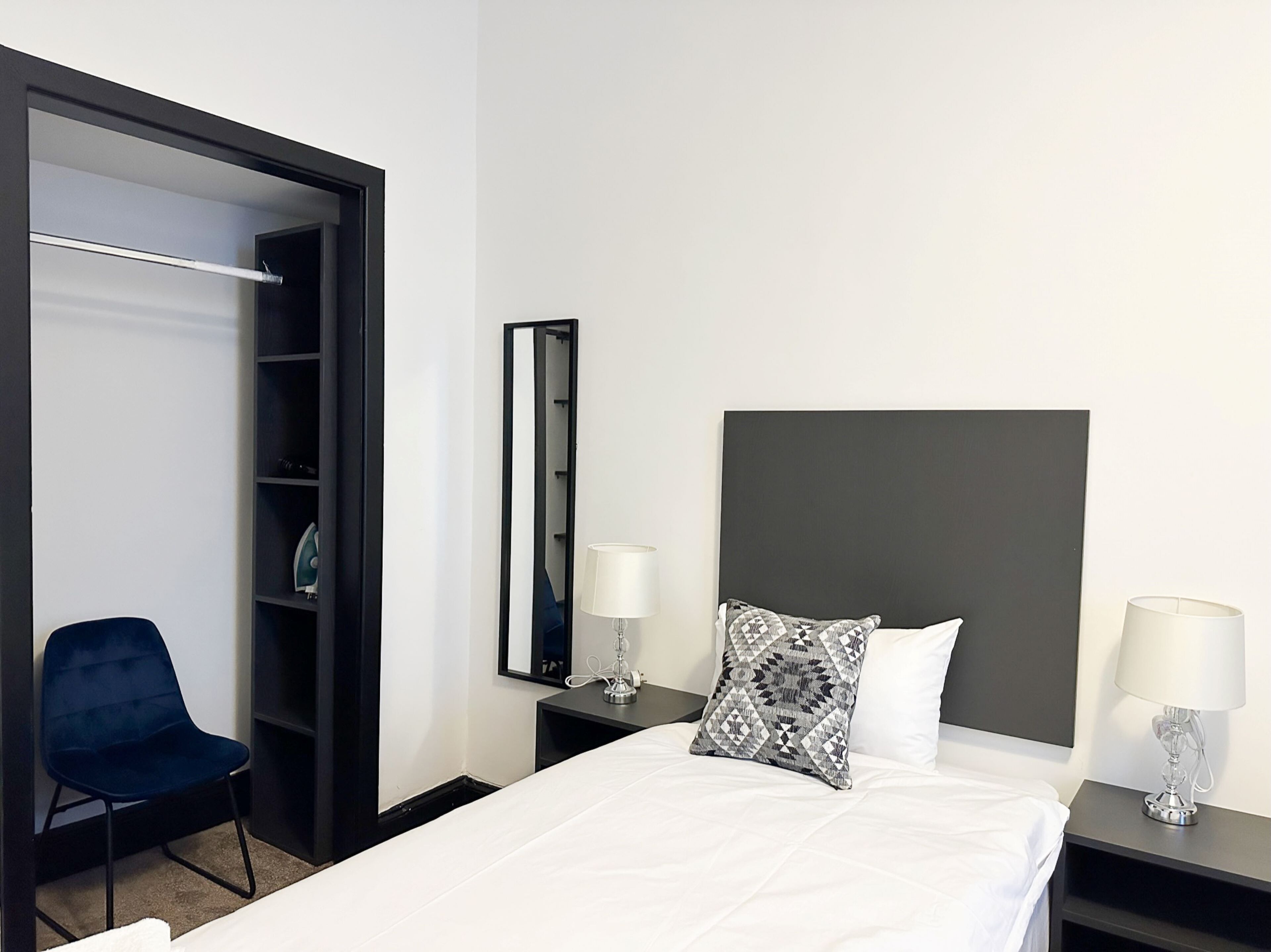 A hotel room with a bed, two bedside tables with lamps, a chair, a wardrobe, and a mirror.