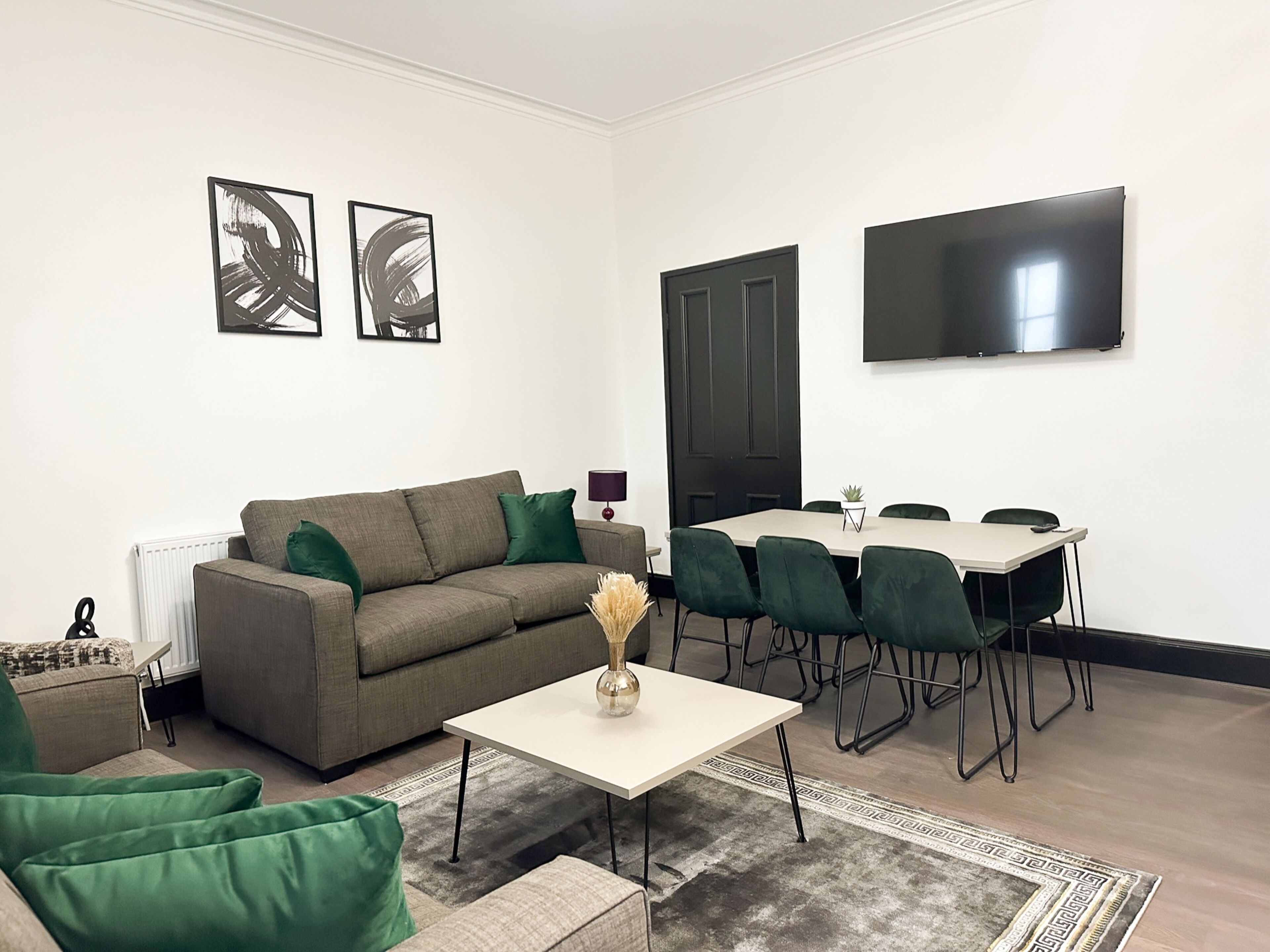 A living room with a sofa, green chairs, a coffee table, and a TV.