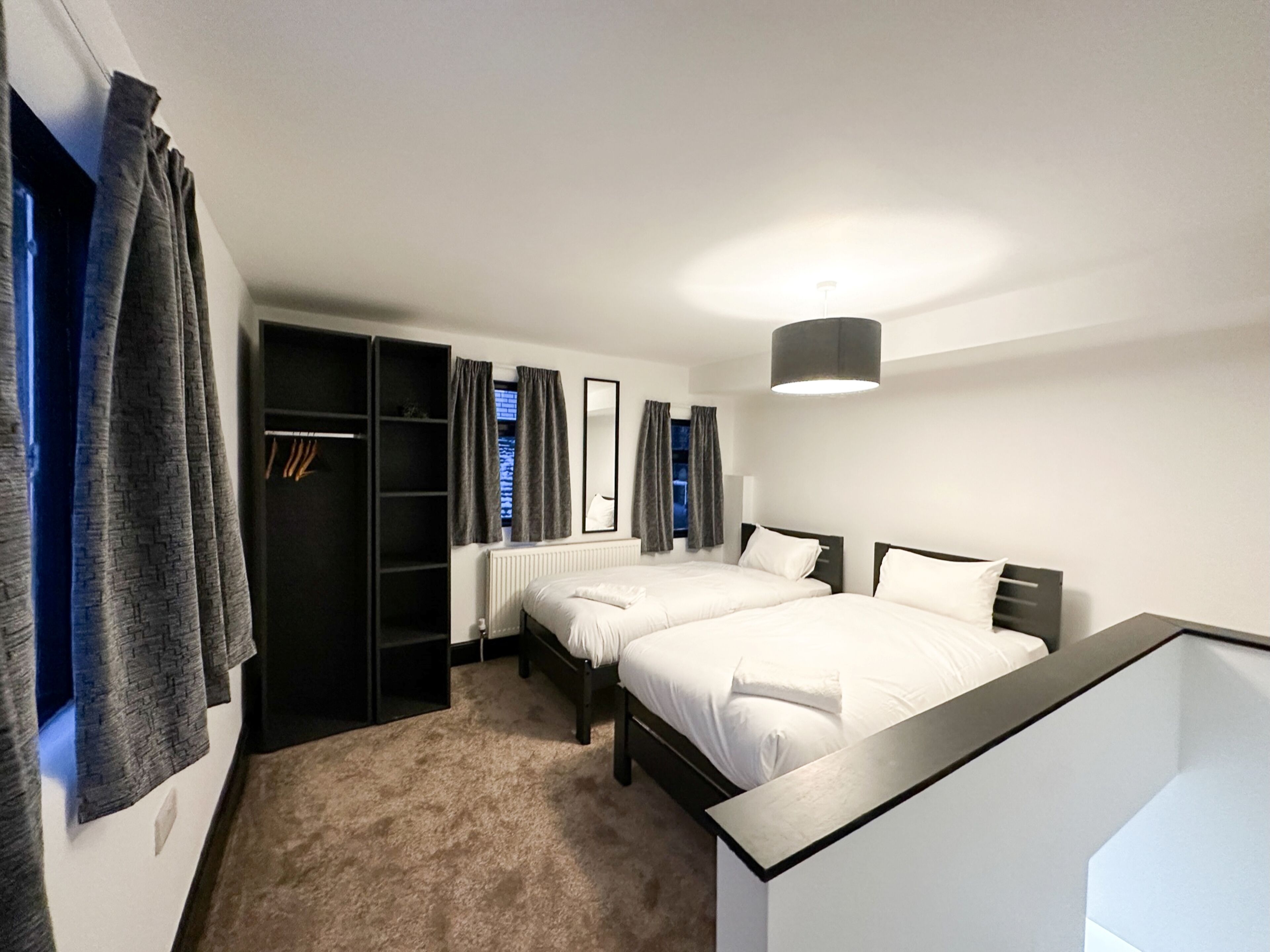 A modern hotel room with two beds, a walk-in closet, and a large window with curtains.