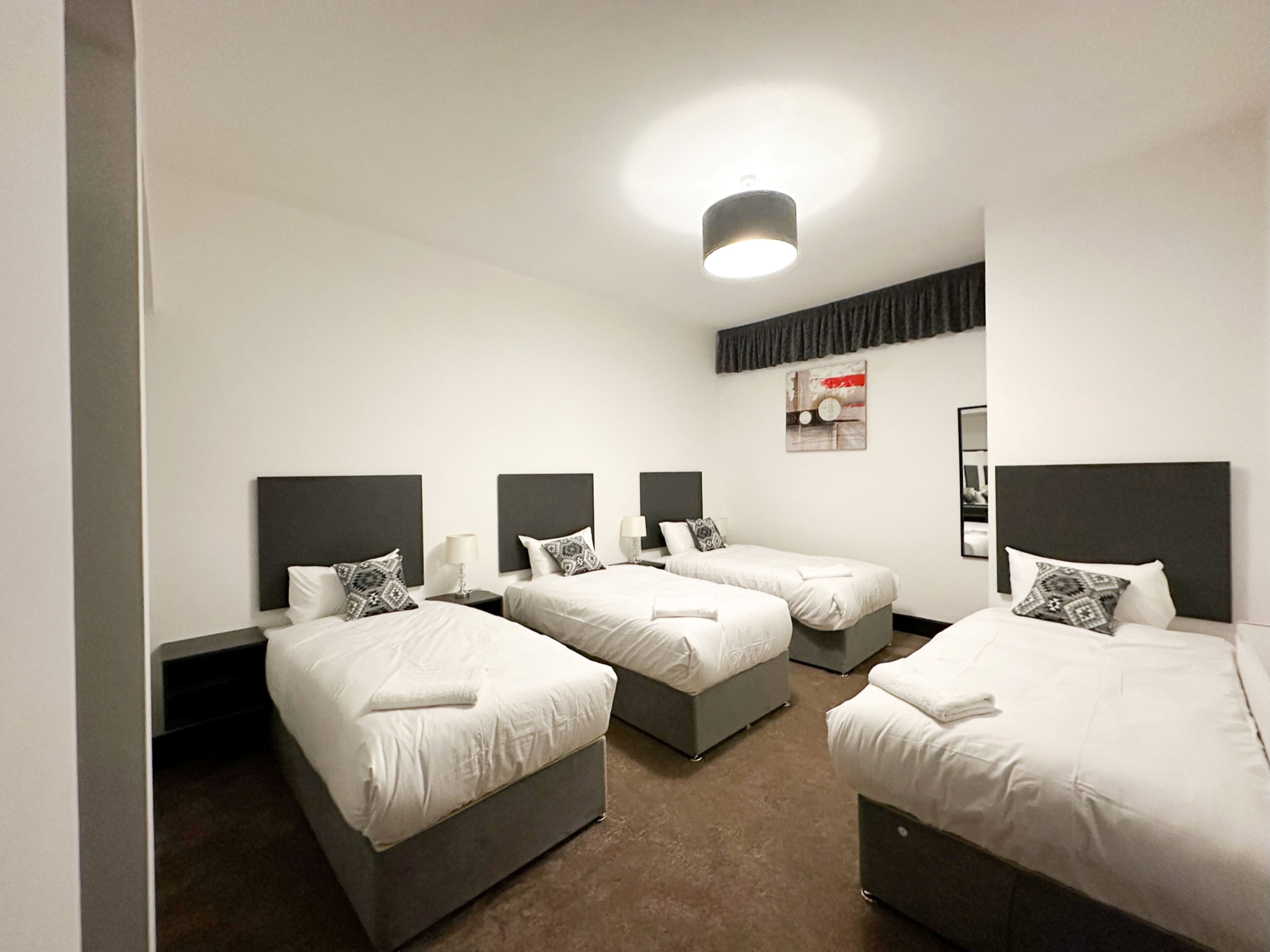 A hotel room with four single beds, a ceiling light, and a framed picture on the wall.
