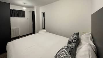 A modern bedroom with a large bed, a bedside table, a mirror, and a radiator.