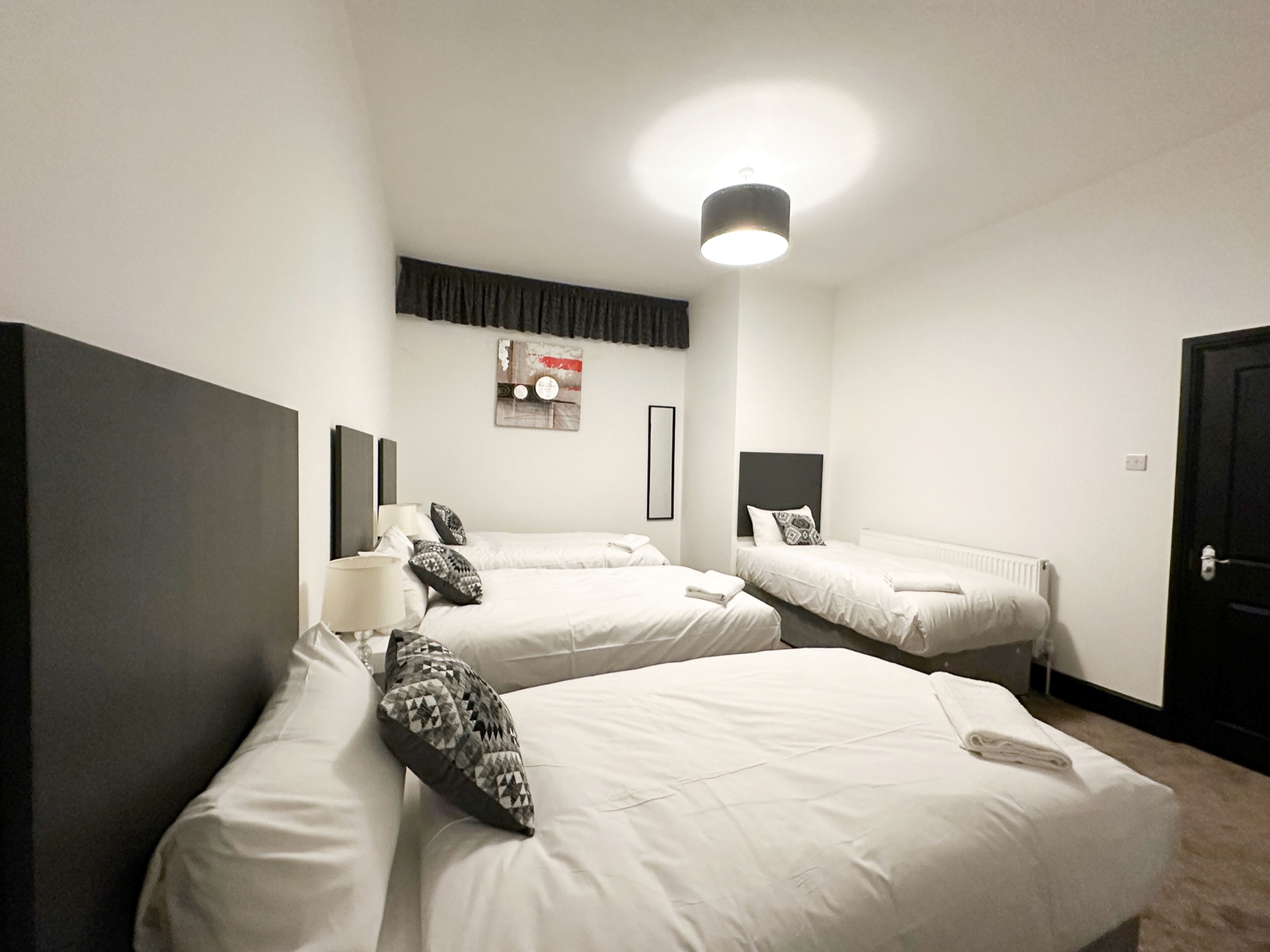 Habitación de hotel con dos camas individuales, un espejo grande, una lámpara en el techo y un cuadro en la pared.