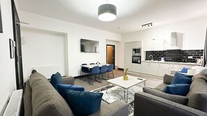 Ein modernes Wohnzimmer mit einer Sofagarnitur, einem Esstisch und einer Küchenzeile mit Schränken und Geräten.