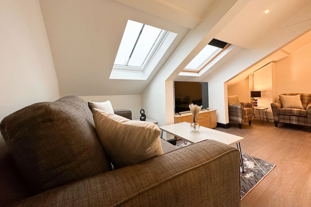 Um apartamento loft moderno com pé-alto, claraboias, um sofá grande, uma mesa de centro e uma televisão.