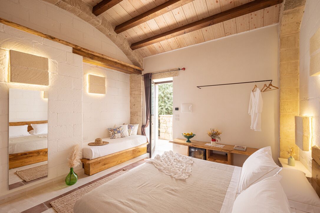 A bedroom with a large bed, a wooden bench, a bedside table, and a mirror.