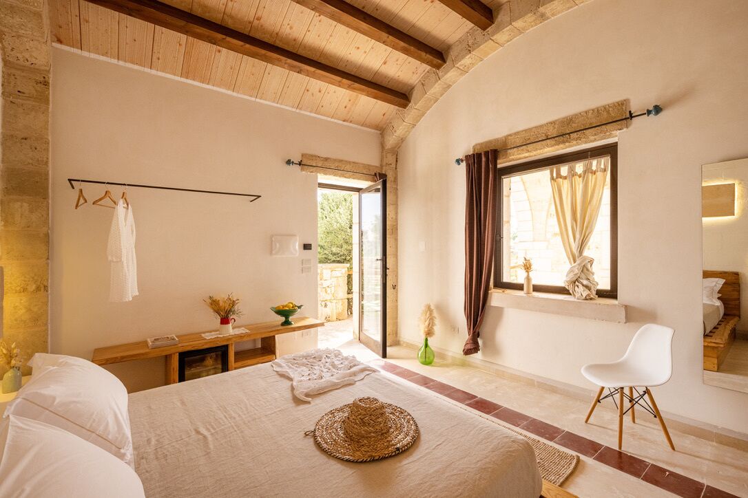 A bedroom with a bed, a bedside table, a chair, a window with curtains, and a view of the outdoors.