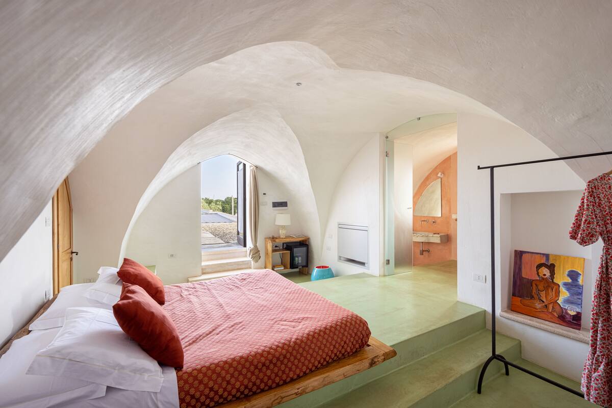 A bedroom with a bed, a painting, and a staircase leading to an adjacent room.