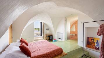 A bedroom with a bed, a painting, and a staircase leading to an adjacent room.