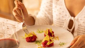 A person dining at a table with a lace tablecloth, a plate of food, and a glass of red wine.