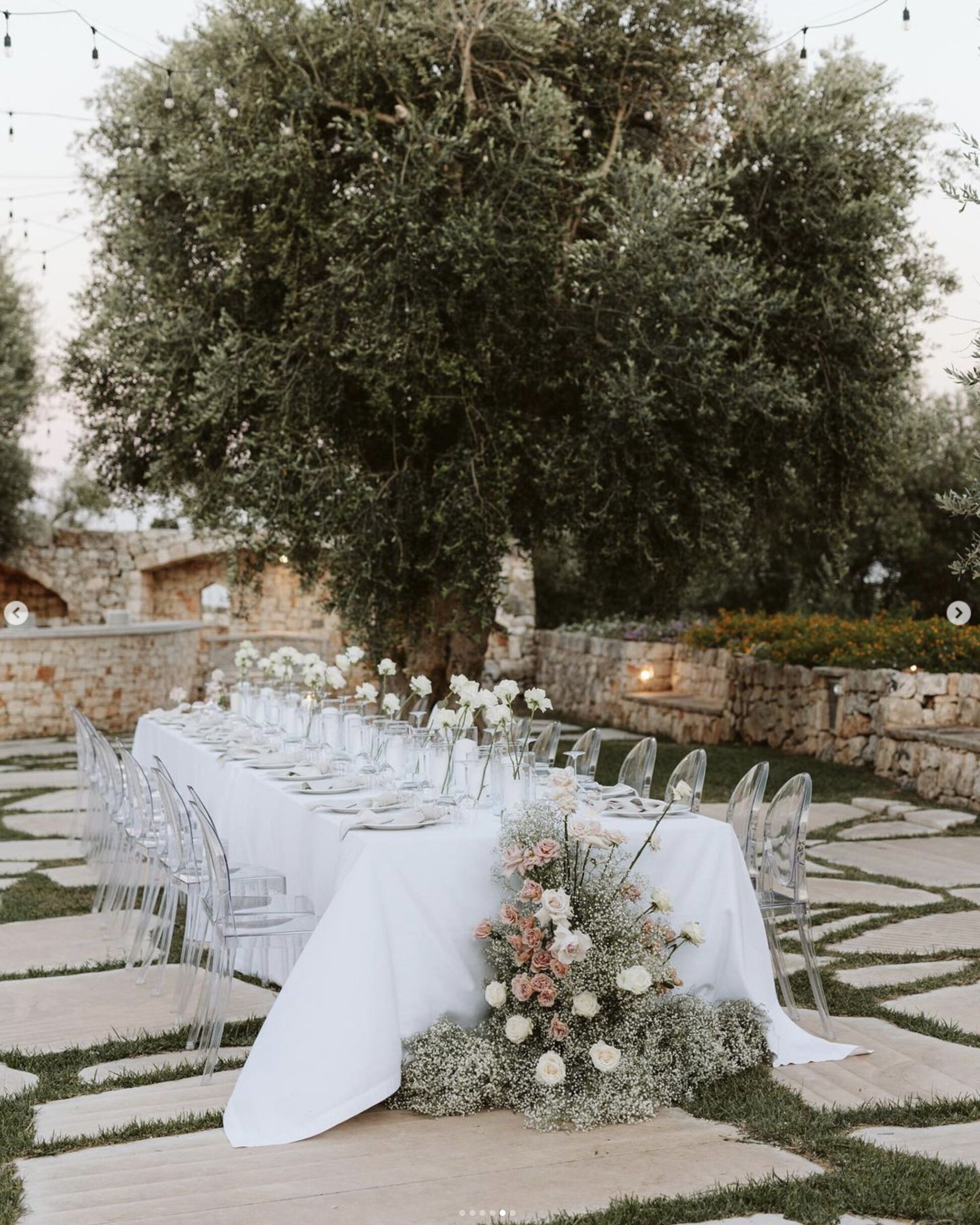 Un área de comedor al aire libre con una mesa larga lista para una comida, rodeada de muros de piedra y follaje.