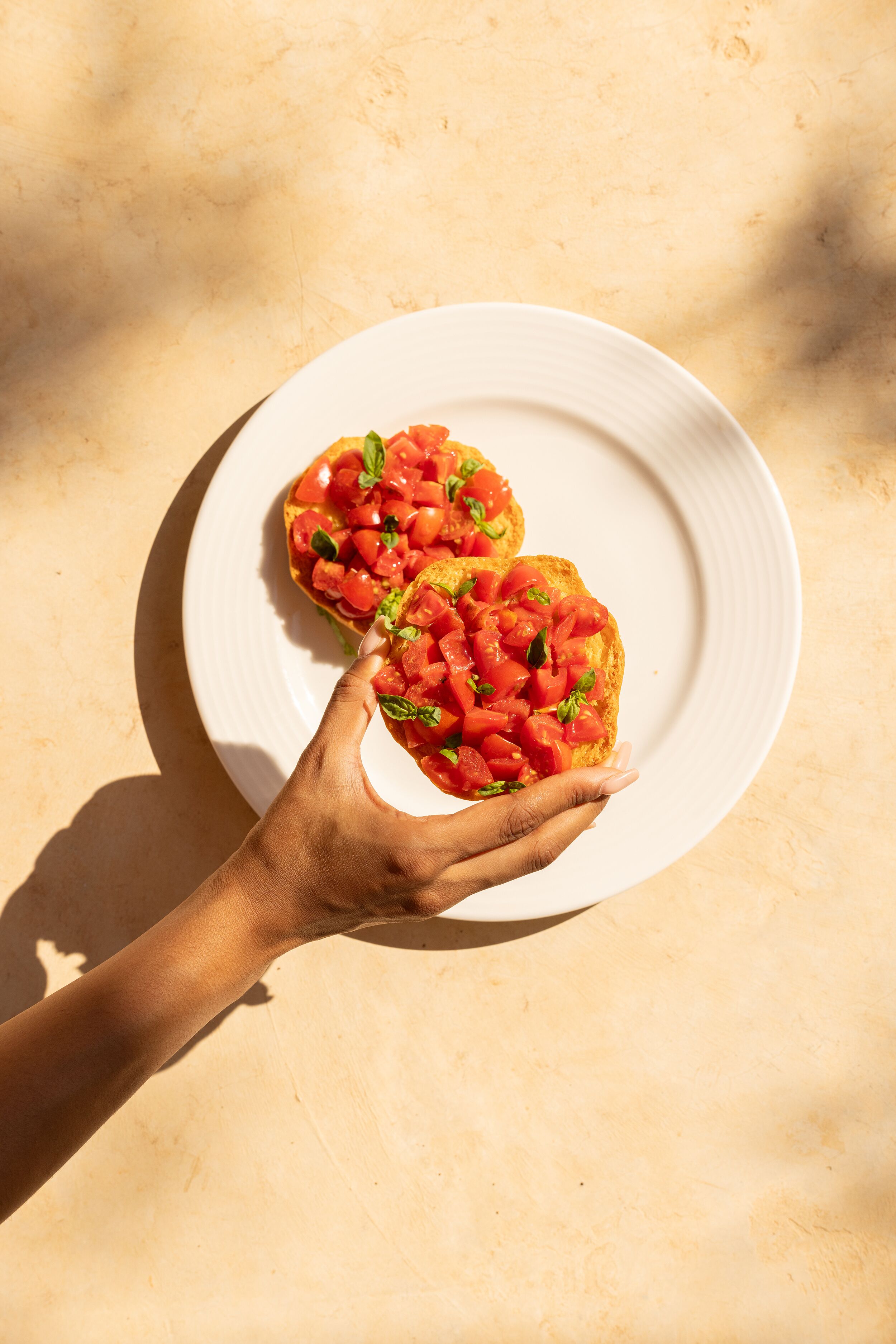 A hand holding a plate with two pieces of toast topped with tomatoes and basil.