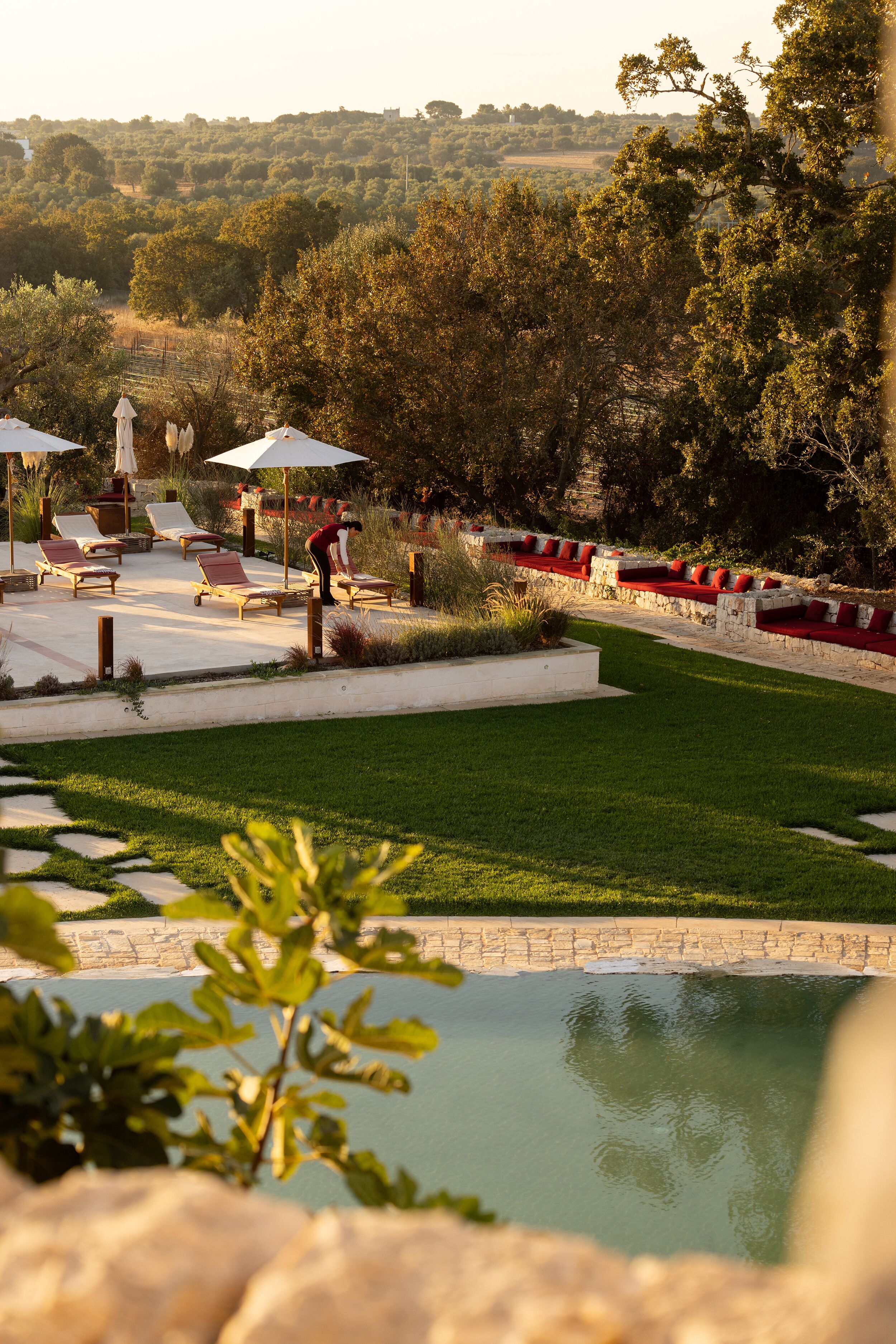 A landscaped outdoor area with a pool, lounge chairs, and a person tending to the grass.