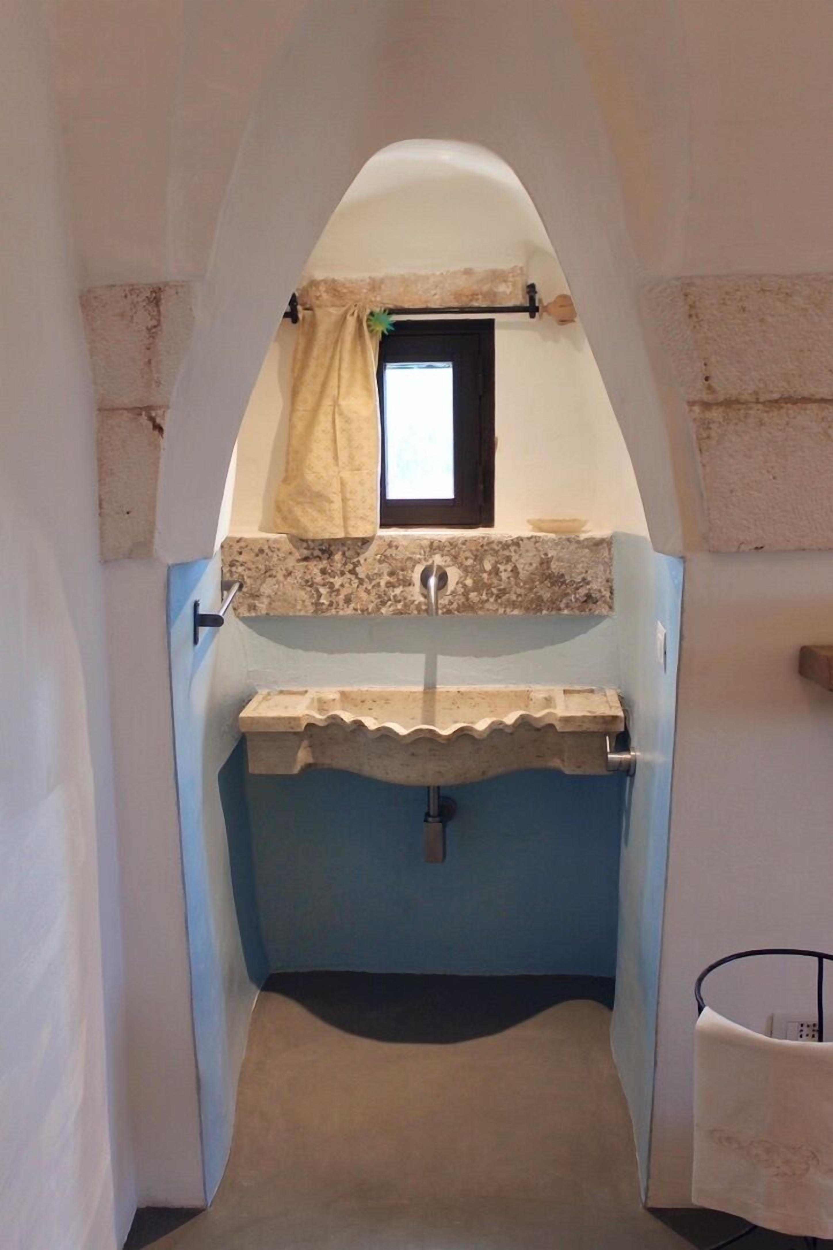 Un baño estrecho con ventana, un lavamanos y un perchero para toallas.