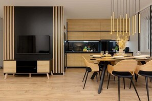 Una cocina moderna con armarios de madera, un mueble para televisor negro y una zona de comedor con sillas y mesa dispuesta para cuatro personas.