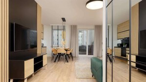 A modern living room with a flat-screen TV, wooden furniture, a dining area, and a green sofa.