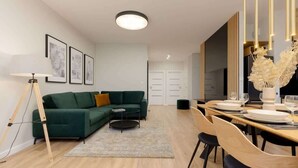 A modern living room with a green sofa, a dining table set for four, and a standing lamp.