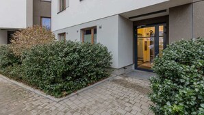 A modern building with a glass entrance, a small garden area, and a paved walkway.