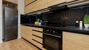 A modern kitchen with wooden cabinets, a black countertop, a built-in oven, and a stainless steel refrigerator.