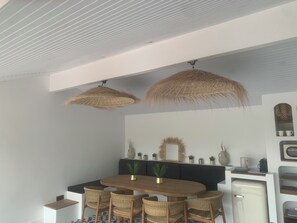 A dining area with a round wooden table, wicker chairs, and two hanging rattan lamps.