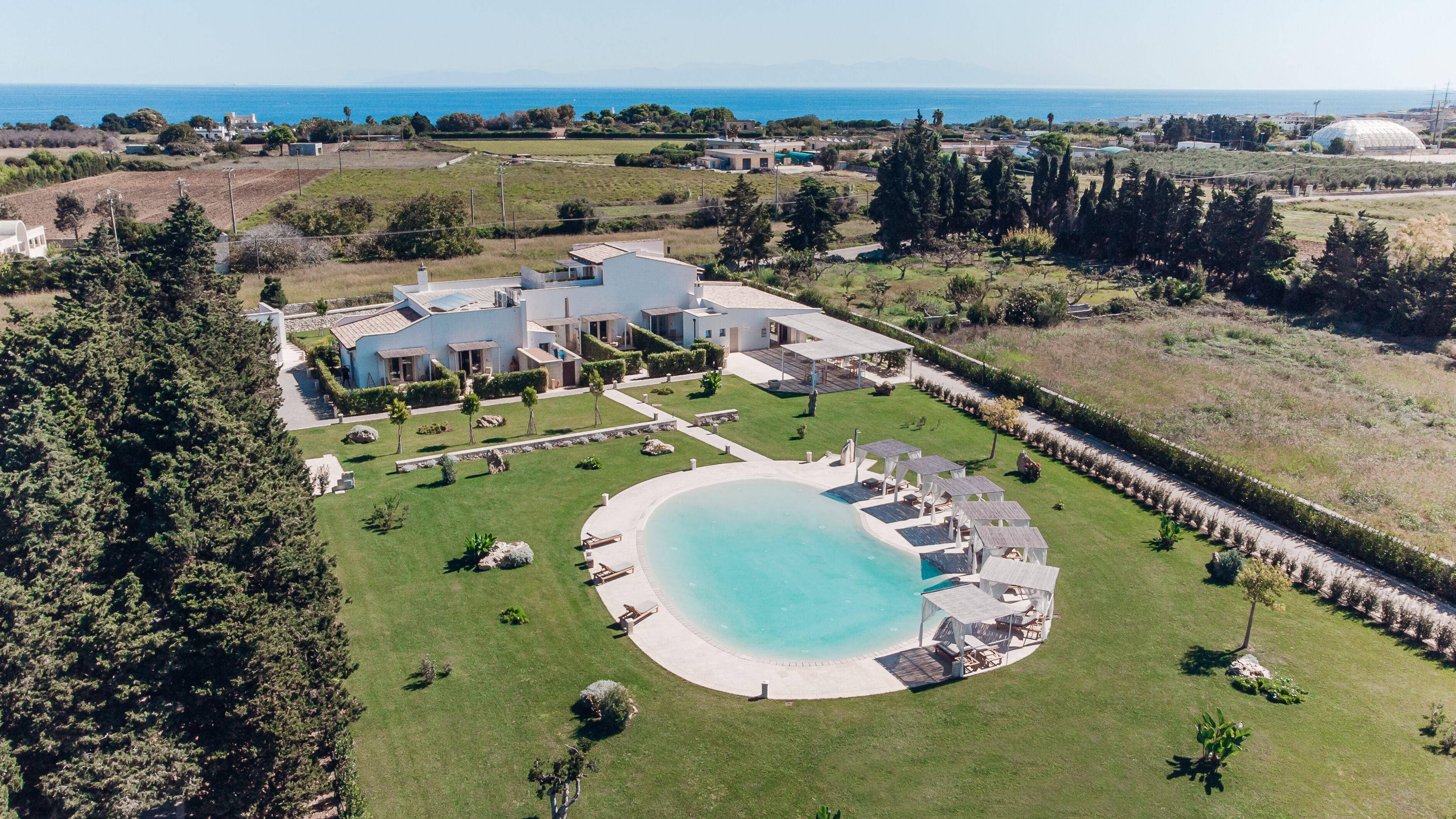 Vue aérienne d’un complexe hôtelier moderne doté d’une grande piscine, de plusieurs bâtiments et offrant une vue panoramique sur l’océan.