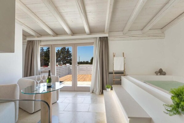 Una sala moderna con una mesa de vidrio, sofá y vistas a una terraza de madera y árboles.