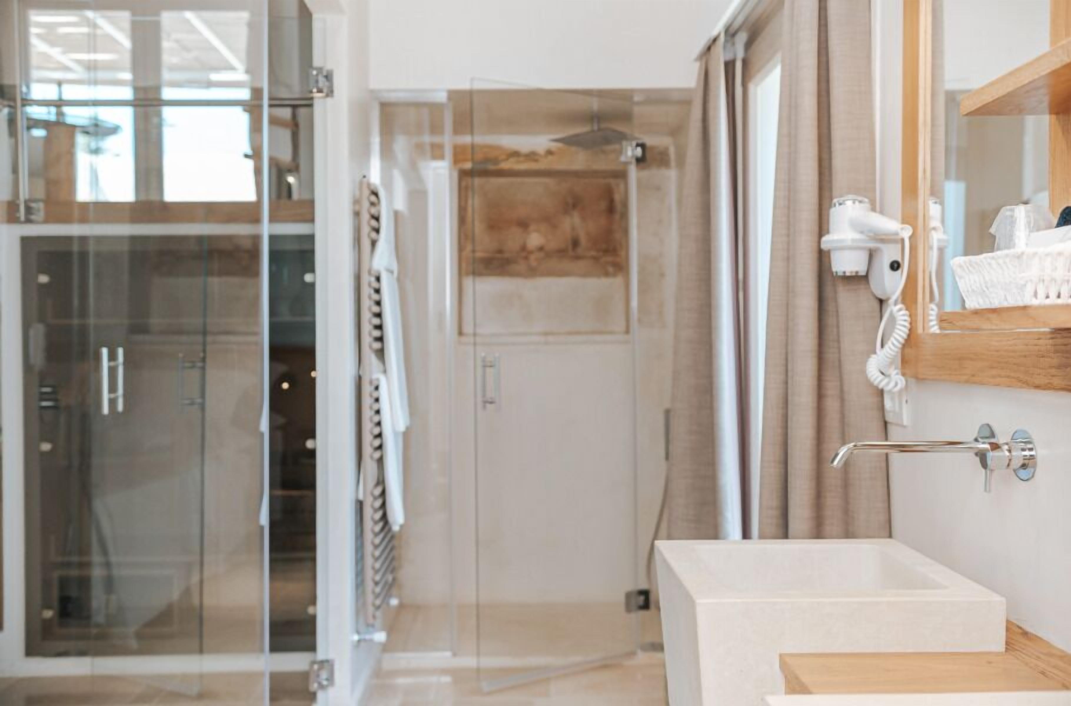 A modern bathroom with a glass shower enclosure, a white sink, and a hairdryer mounted on the wall.
