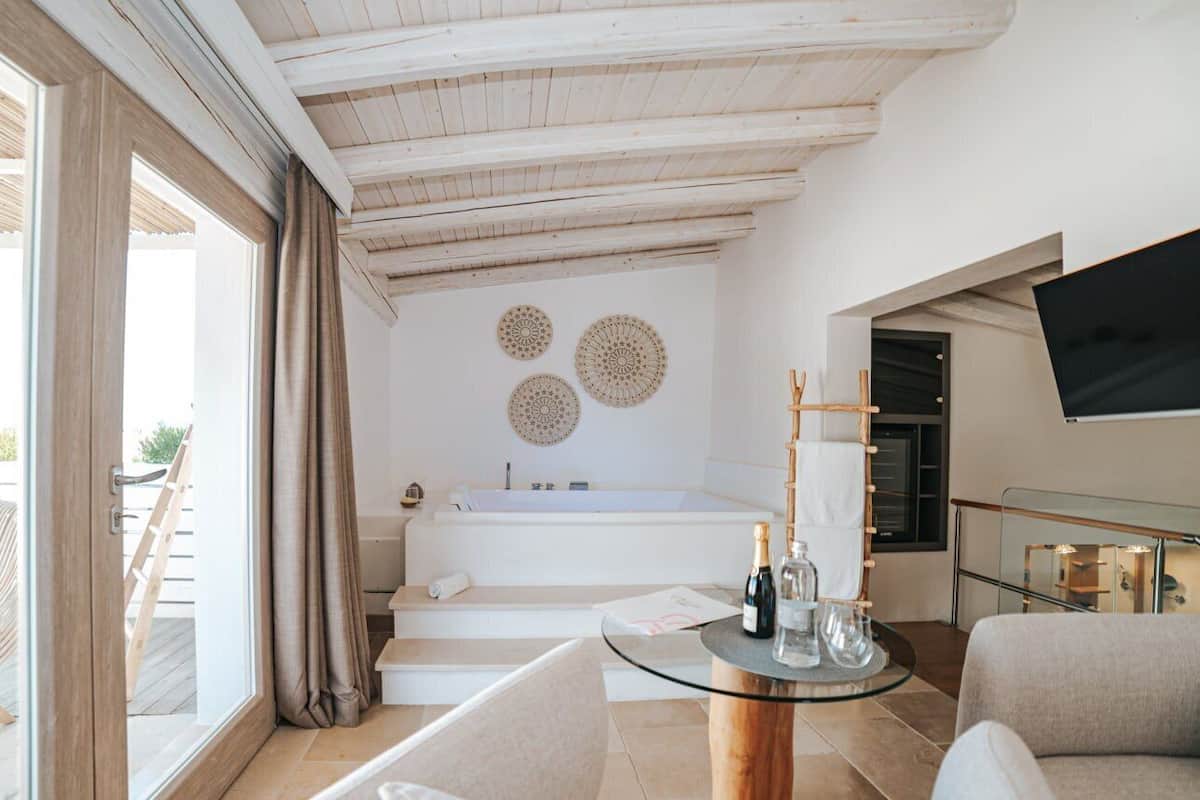 A modern bathroom with a bathtub, a glass table with bottles, and a TV on the wall.