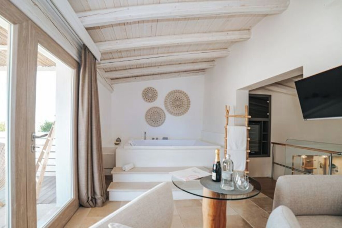 Un baño moderno con una bañera, una mesa de vidrio con botellas y un televisor en la pared.
