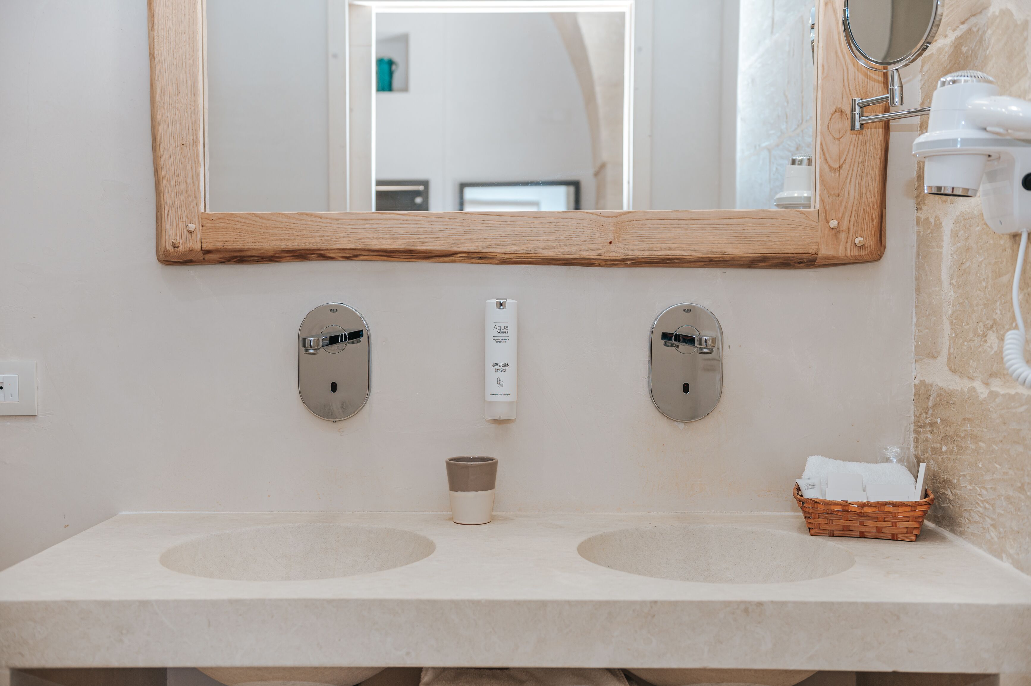 A bathroom with two sinks, a wooden-framed mirror, a hairdryer, and a basket of towels.