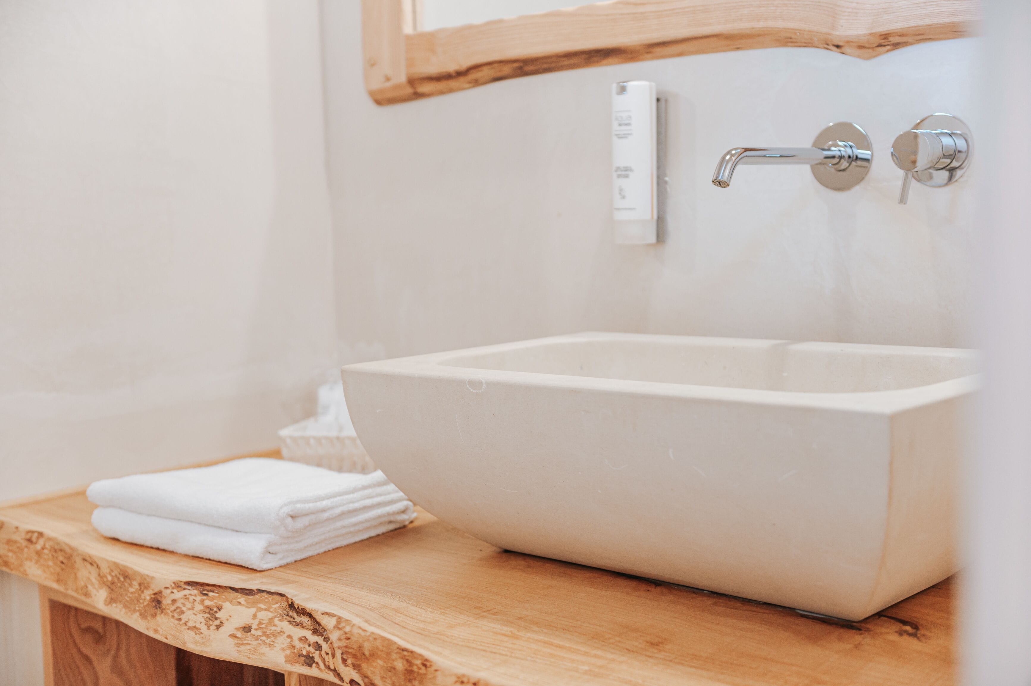 A bathroom with a large, white vessel sink, a wooden countertop, and a wall-mounted faucet.