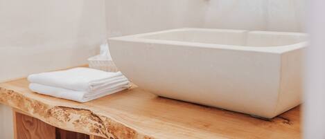 A bathroom with a large, white vessel sink, a wooden countertop, and a wall-mounted faucet.