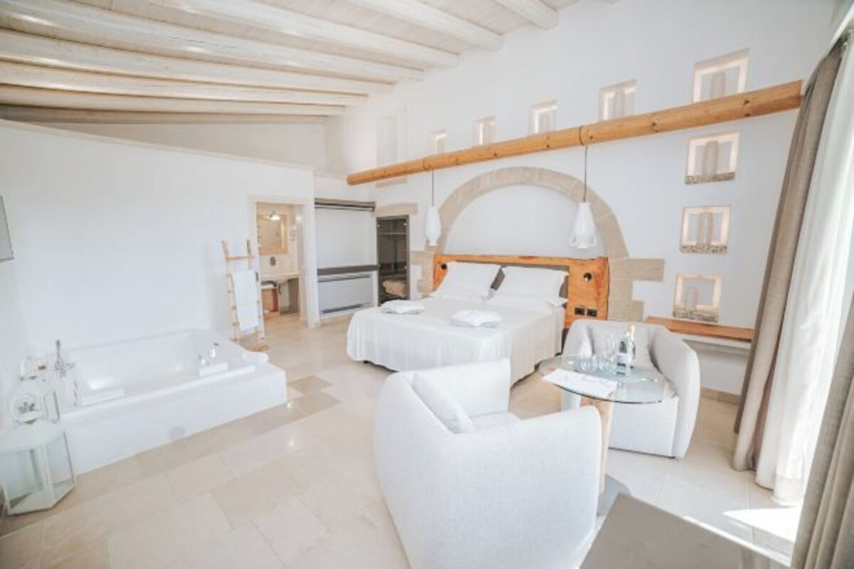 Habitación de hotel moderna con una cama grande, un sofá independiente, una mesita pequeña y una bañera.