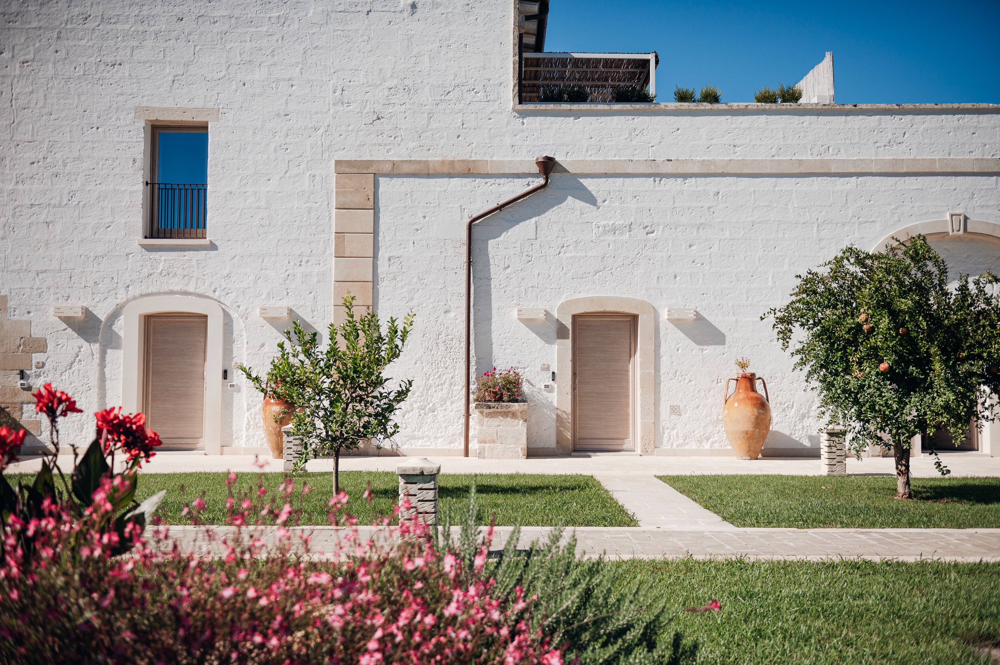 Un edificio blanco con una ventana pequeña, dos puertas y un jarrón grande.