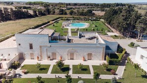 Un gran edificio con piscina, rodeado de césped cuidado y árboles.