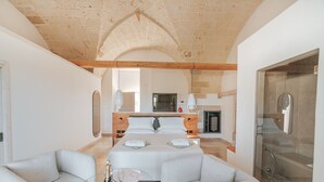 Un dormitorio amplio con una cama grande, un rincón de descanso con una mesa de vidrio y un área de ducha.
